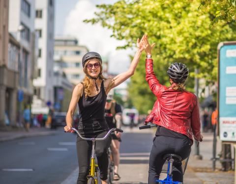 Kaksi pyöräilijää ajaa toistensa ohi ja läpäyttää toista kädellään tervehdykseksi.