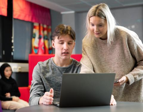 Nuori kannettavan äärellä, aikuinen vieressä opastaa.