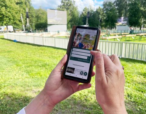 Sorsapuistossa oleva ihminen selaa tapahtumakalenteria kännykällään. Ihmisestä näkyvät vain kädet.