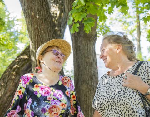 Kaksi henkilöä katsoo toisiaan hymyillen seisten puun alla.
