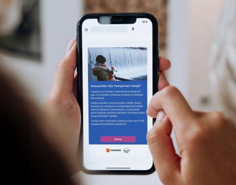 Kädet pitelemässä älypuhelinta, jonka näytöllä näkyy rekrypelin avausnäkymä.