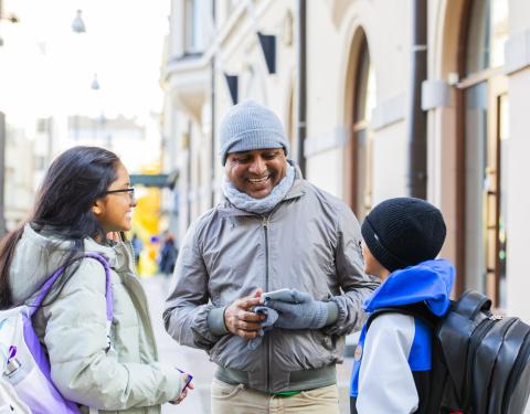 Kaksi aikuista ja lapsi juttelevat kadulla.