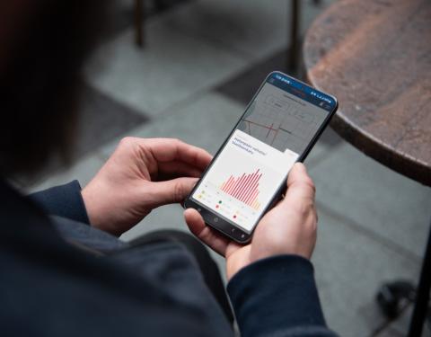 Henkilön kädessä puhelin, jonka ruudulla näkyy datakäyrä. 