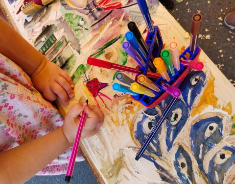 Kädet piirtävät puiseen lankkuun, jonka päällä on kyniä.