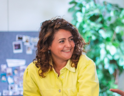 Woman is sitting at a table. She is having a cup of coffee and is smiling.