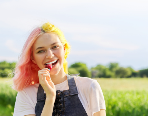 Teini-ikäinen tyttö on maalaismaisemassa ja maistaa mansikkaa. Kuvassa on keltainen leima, jossa lukee kesätyöseteli.