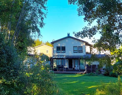 Vaalea omakotitalo puistoisessa maisemassa.