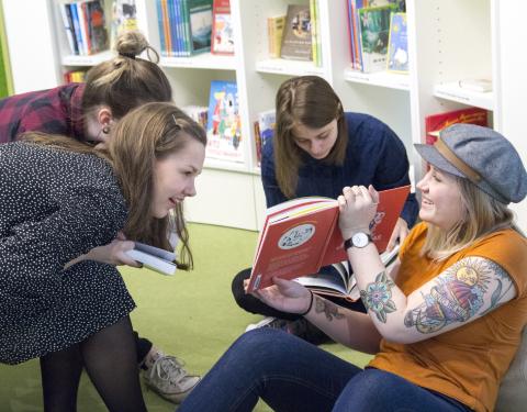 Neljä nuorta istuu ja katsoo muumikirjaa, taustalla kirjahylly.