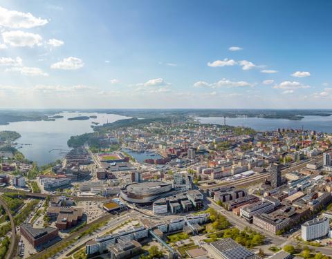 Tampereen kaupunkialue ilmasta käsin kuvattuna, etualalla tiivistä kaupunkia ja taustalla siintää järvimaisema.