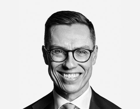 Hymyilevä Alexander Stubb kuvattuna vaaleaa taustaa vasten, päällä puku, lyhyet hiukset ja silmälasit.
