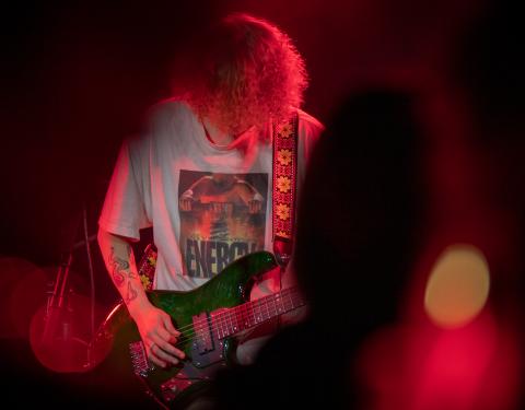 henkilö soittaa kitaraa punaisessa valaistuksessa.