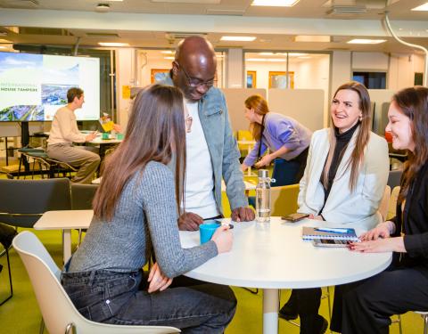 Neljä hymyilevää, eri etnisiä ryhmiä edustavaa ihmistä keskustelemassa pöydän ääressä.