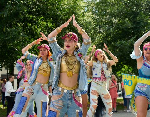 Värikkäästi pukeutuneita naisia tanssimassa kädet ylhäällä pään päällä.