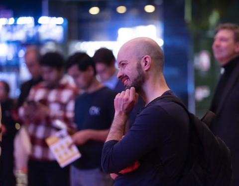 Hymyilevä asukas katselee esitystä tamperelaisten illassa. Hän koskee kädellä leukaansa.