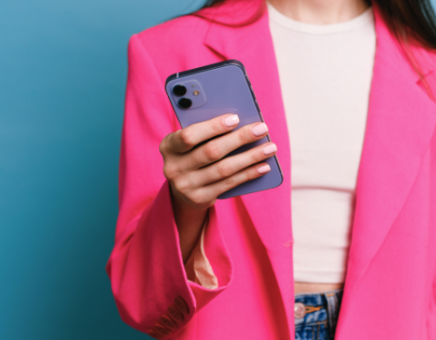 Henkilö pitelee kädessään violettia kännykkää. Hänellä on päällään pinkki jakku.