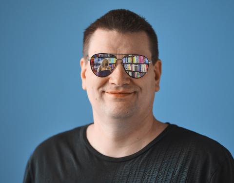 Keski-ikäinen mies katsoo kohti. Hänen aurinkolaseistaan heijastuu kuva kirjastosta.