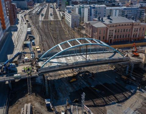 Kuvassa vaaleansininen silta radan päällä ja työkoneita,