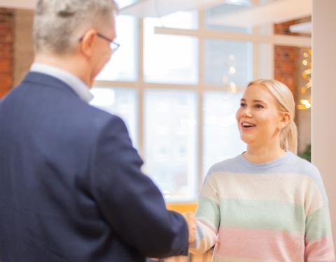 Kaksi henkilöä kättelee ja hymyilee toisilleen toimistorakennuksessa.