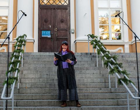 Nainen seisoo portailla ja lukee käsissään pitelemästään kansiosta runoa.