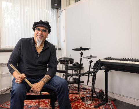 A man is sitting by a drum set and smiling to a camera