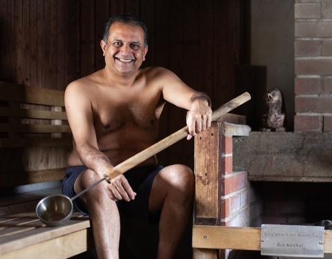 Indian man sits in a sauna, smiling to a camera
