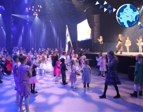 Lapsia tanssimassa lavan edessä. Lavalla tanssinohjaajia opastamassa tanssimaan. 