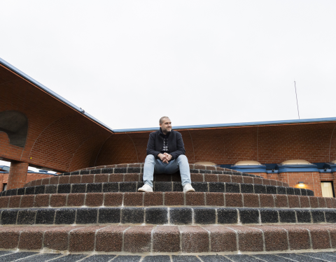 Henkilö istuu punatiilisen rakennuksen edessä portailla.