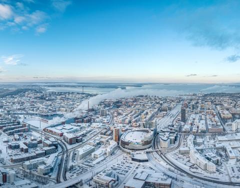 Ilmakuvassa levittäytyy luminen Tampere. Keskellä Nokia Arena ja risteilevät tiet, taustalla järvet ja sininen taivas.