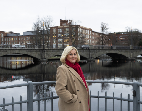 Henkilö seisoo metallikaiteen edessä. Takana näkyy koskea, Satakunnansilta autoineen ja Tampellan rakennuksia.