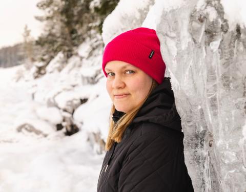 Punapipoinen henkilö nojaa jäiseen korkeaan kallioon.