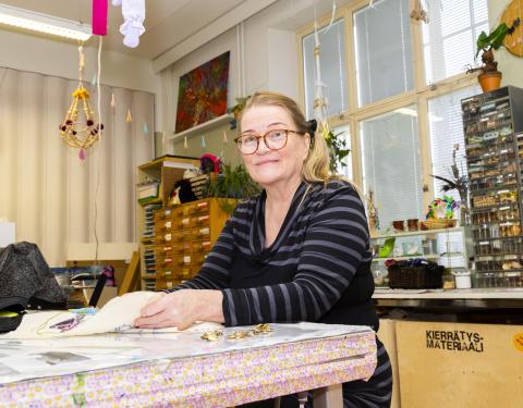 Raitapaitainen nainen tekee käsityötä Monitoimitalon kädentaitopajassa.