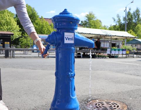 Naisen käsi päästää vesipostista vettä Tammelantorilla.