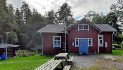 Punainen puutalo, pihalla pöytäpenkkiryhmiä