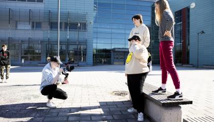 Opiskelija ottaa valokuvaa kolmesta opiskelijasta pihalla.