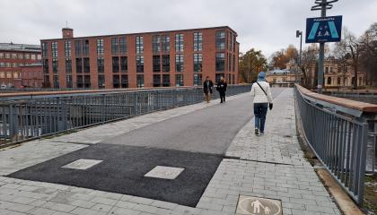 Palatsinraitin silta, jolla näkyy opastekyltti sekä tiemerkintälaatat, jotka kertovat missä kohtaa siltaa ovat kävelijöiden ja pyöräilijöiden paikat.