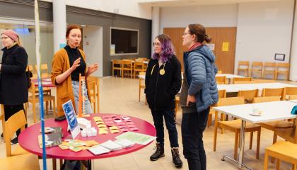 Kaupungin työntekijä seisoo pyöreän pöydän ääressä ja kertoo kahdelle asukkaalle kaupungin ajankohtaisia asioita.