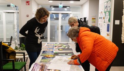 Kaupungin työntekijä kumartuu esittelypöydän ylitse katsomassa yhdessä asukkaiden kanssa pöydällä olevia aineistoja.