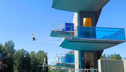 Lapsi hyppää maauimalan hyppytornista aurinkoisena kesäpäivänä.