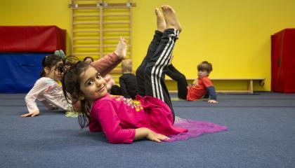 Pikkutyttö makaa jalat kohti kattoa jumppa-alustalla.