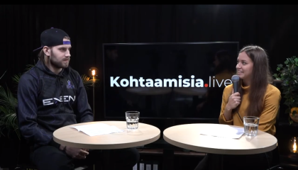 Nainen mikrofonin kanssa haastattelee miestä kahden pyöreän pöydän äärellä