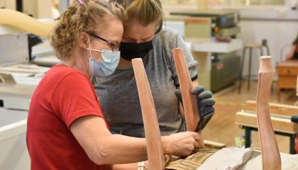 Kaksi henkilöä entisöi tuolia puukäsityöluokassa.