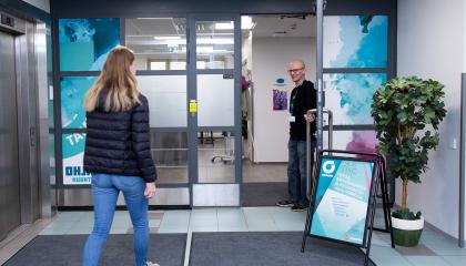 Työntekijä pitää ovea auki. Nuori henkilö on astumassa sisälle.