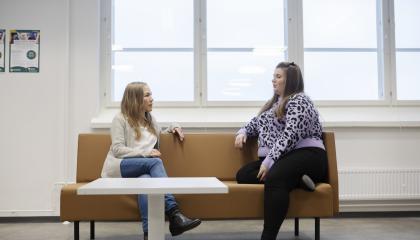 Kaksi henkilöä istuu sohvalla ja juttelee keskenään.