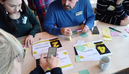 Neljä henkilöä työskentelevät pöydän äärellä työpajassa.