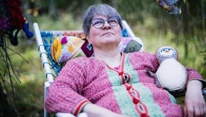 Henkilö istuu lepotuolissa puutarhassa. Hänellä on kainalossaan itse tehty käsityöpehmolelu.