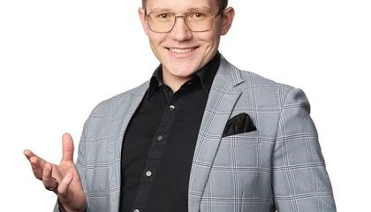 Tummahiuksinen mies seisoo kuvassa puvuntakki päällään ja hymyilee kameralle