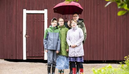 Lantelankallion perhe seisoo punaisen varaston edessä punaisen sateenvarjon alla.