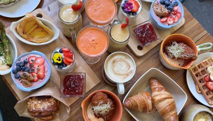 Pöydälle on katettu erilaisia ruokia kuten esimerkiksi puuroa, croisantteja, kahveja, vohveleita ja marjoja.