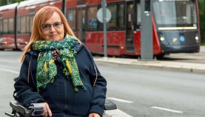 Rita Järvinen sitting in a wheelchair on the street, with a tram in the background.