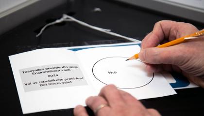 Äänestyslipuke vaalikopin pöydällä ja kaksi kättä, joista toisessa on lyijykynä.